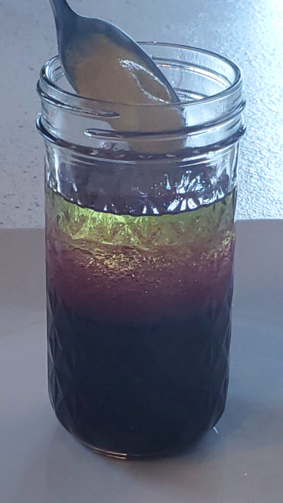 A mason jar is filled with the ingredients for this Delicious 3-Ingredient Pomegranate Vinaigrette before it is capped, shaken and ready to drizzle over a fresh salad.