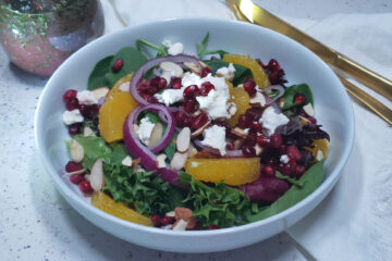 A salad of fresh greens, oranges, pomegranate arils, red onion, goat cheese crumbles and almonds is topped with this Delicious 3-Minute Pomegranate Vinaigrette