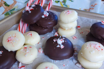A tray of these Easy 4-Ingredient Minze Patties. Some of the peppermint patty candies are dipped in dark chocolate, others in white chocolate. Candy cane sprinkles decorate the tops.