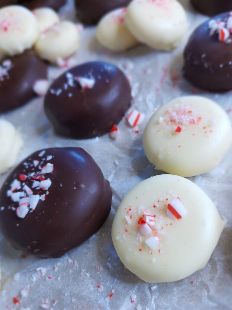 A tray of these Easy 4-Ingredient Minze Patties. Some of the peppermint patty candies are dipped in dark chocolate, others in white chocolate. Candy cane sprinkles decorate the tops.