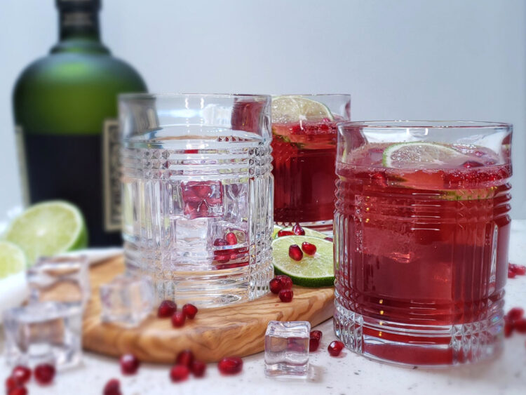 A glass of this Simple 5-Ingredient Rum Pom Punch is served well chilled over ice and topped with a fresh slice of lime and pomegranate arils.
