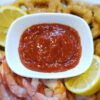 A bowl of this Simple and Delicious 4 Ingredient Cocktail sauce is surrounded by cooked shrimp and calamari rings for dipping.