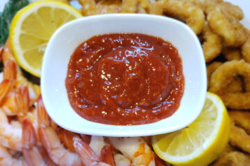 A bowl of this Simple and Delicious 4 Ingredient Cocktail sauce is surrounded by cooked shrimp and calamari rings for dipping.