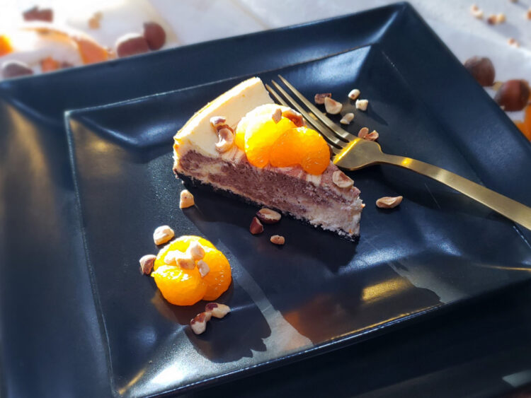 A slice of this Decadent 2 Layer Orange Nutella Cheesecake is topped with fresh oranges and toasted hazelnuts.