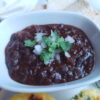 A bowl of these delicious and Easy Black Beans de la Olla in Under 1 Hour is topped with fresh onion and cilantro.