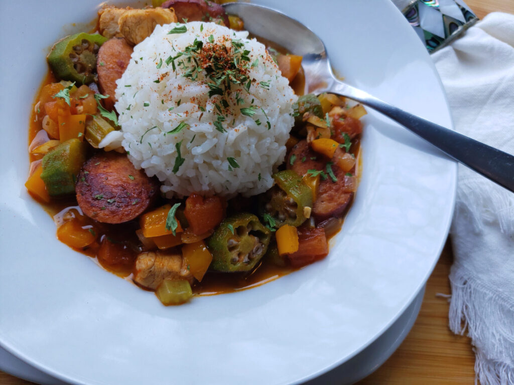A bowl of this Super Simple Chicken and Sausage Jambalaya in 1 Hour sits at the center of a tray. The spicy stew is packed with vegetables, chicken and sausage and topped with a generous scoop of white rice.