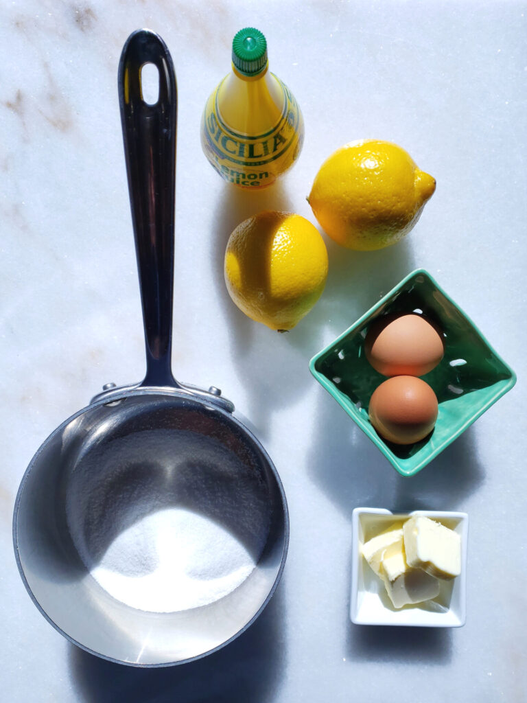 The ingredients for this Quick and Easy 4-Ingredient Lemon Curd are featured on a cutting board. Sugar, lemon juice, butter and eggs.