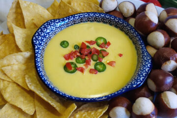 A bowl of this Quick and Easy 5 Minute Queso Dip is surrounded by tortilla chips on the left and pretzel bites on the right.