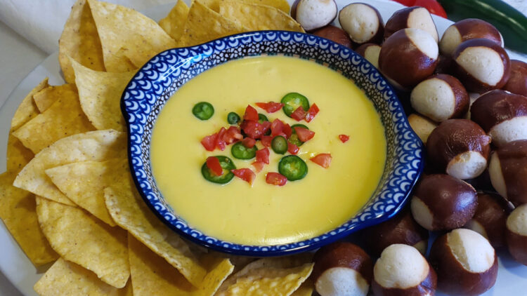 A bowl of this Quick and Easy 5 Minute Queso Dip is surrounded by tortilla chips on the left and pretzel bites on the right.