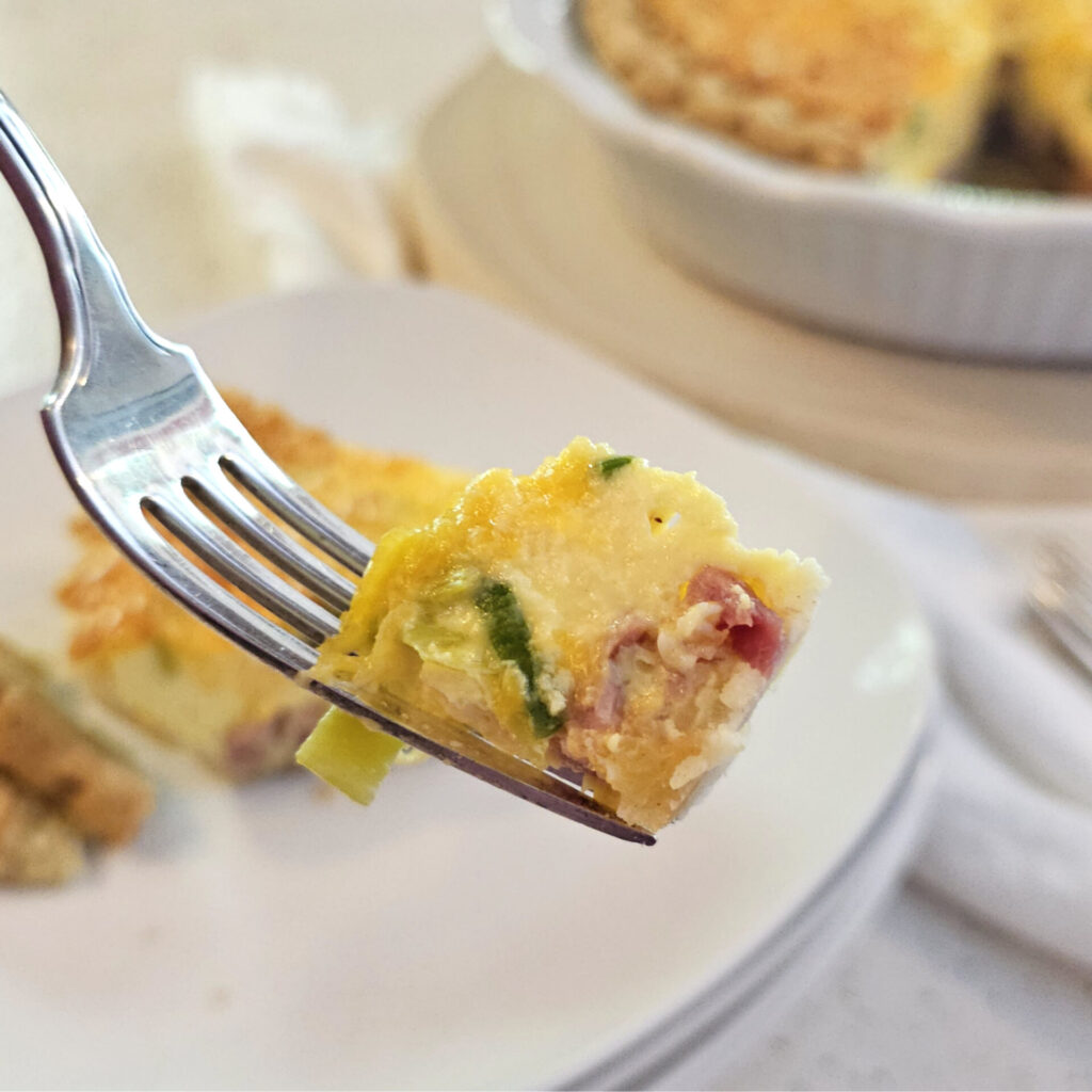 A closeup bite of this Easy 5 Star Homemade Quiche in 90 Minutes reveals ham, leeks and Gouda cheese.