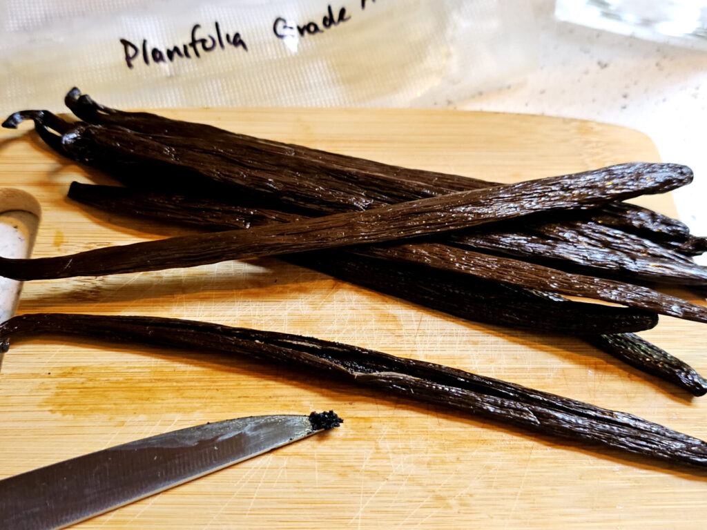Several plump Mexican Planifolia Vanilla pods are payed out on a cutting board and featured in this recipe on How to Make Homemade Pure Vanilla Extract in 5 Easy Minutes.