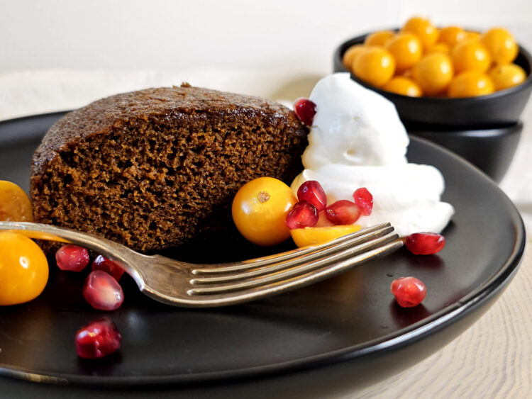 A slice of this moist, tender Festive 5 Star Homemade Gingerbread Cake is served with a dollop of whipped cream, tart gooseberries and pomegranate arils.