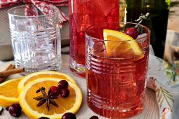 A pitcher of this festive Easy 30 Minute Sparkling Wassail sits neatly on a serving tray with glasses that are garnished with fresh orange slices.