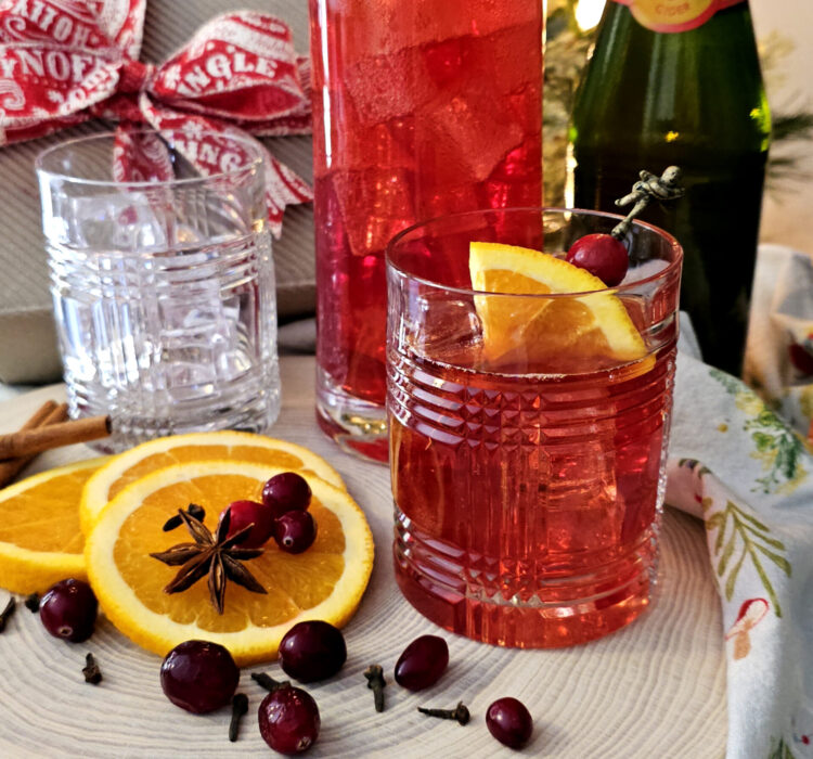 A pitcher of this festive Easy 30 Minute Sparkling Wassail sits neatly on a serving tray with glasses that are garnished with fresh orange slices.