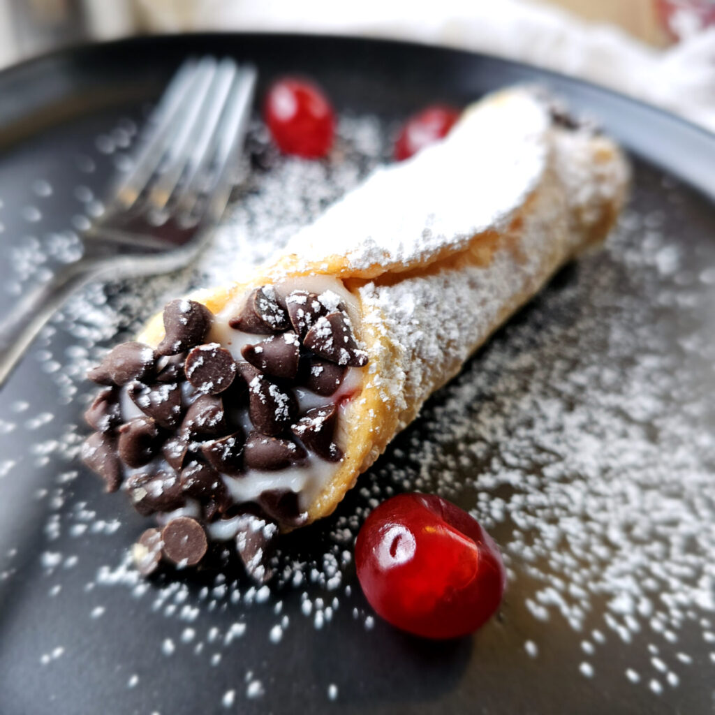 A cannoli sits center of plate and dusted in powdered sugar in this image for Easy as 1-2-3 Chocolate Cherry Cannoli.