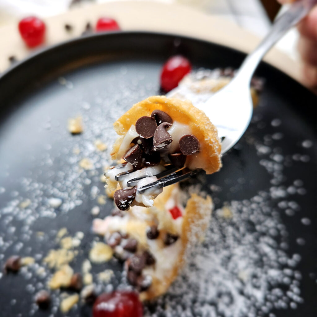 A cannoli sits center of plate and dusted in powdered sugar in this image for Easy as 1-2-3 Chocolate Cherry Cannoli.