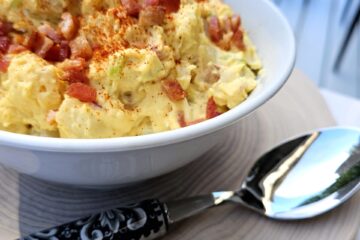A bowl of Old Fashioned Mustard Potato Salad is topped with crispy bacon crumbles and Paprika.