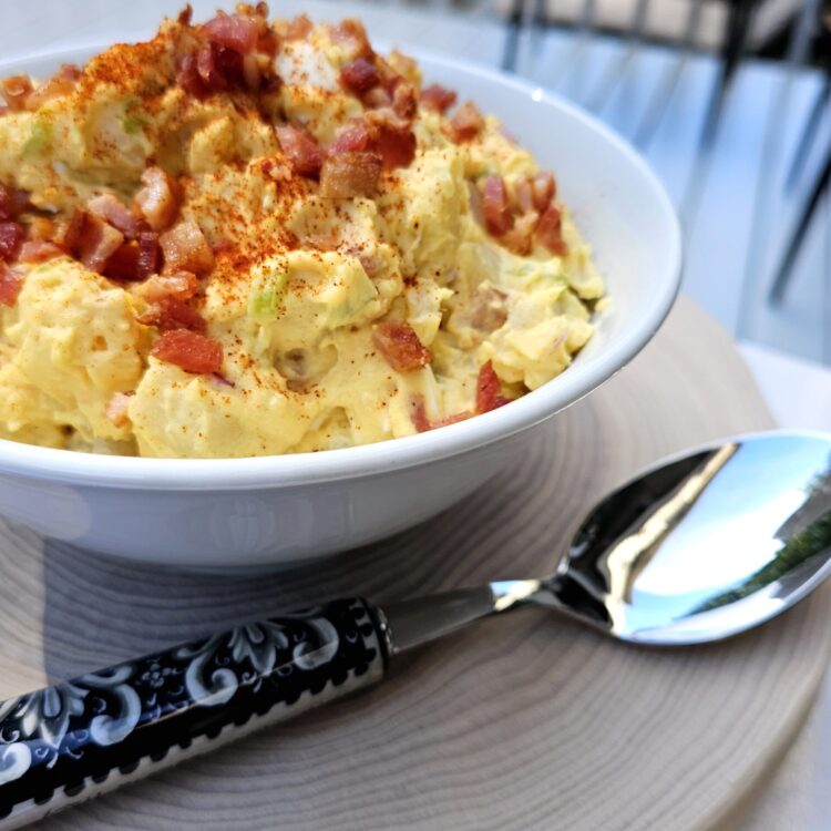 A bowl of Old Fashioned Mustard Potato Salad is topped with crispy bacon crumbles and Paprika.