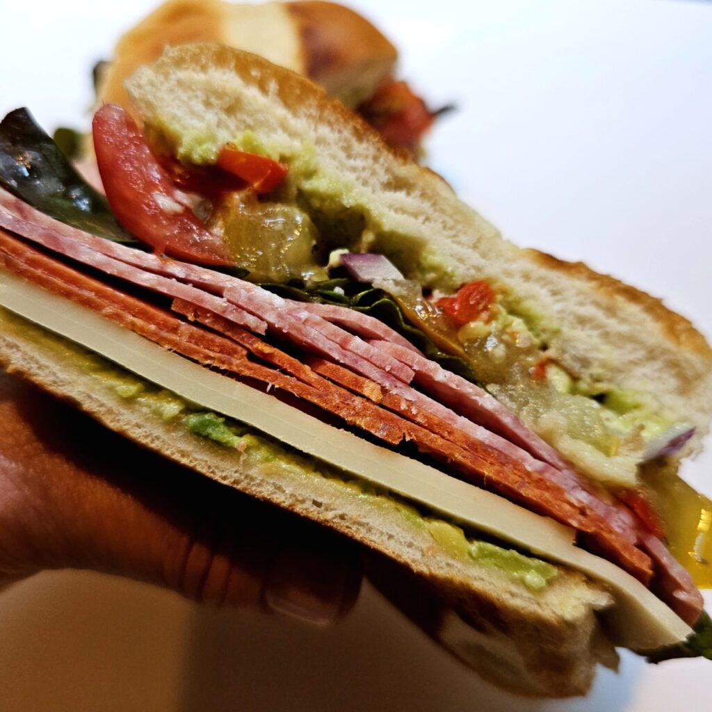 A sandwich made with this Easy Sweet and Spicy Avocado Sandwich Spread is cut in half to show the layers of ingredients.