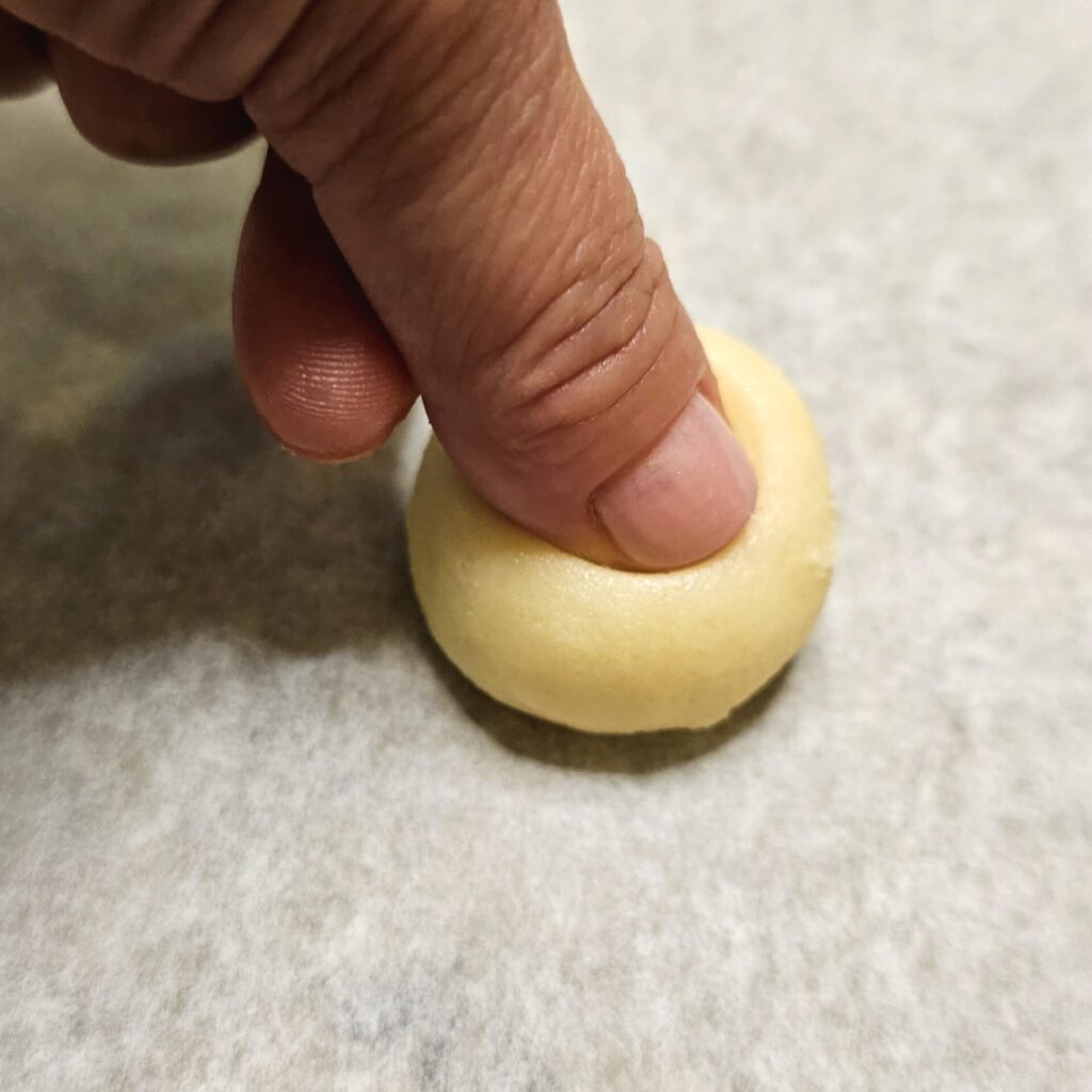 Maria demonstrates how to make a 1/4-inch imprint with her thumb into the top of the cookie dough ball. This imprint is what holds the mango jam in place while baking.