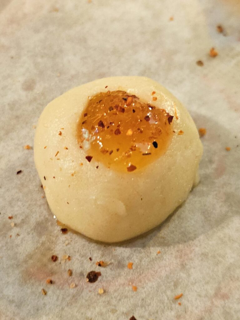 A thumbprint sits filled, sprinkled with Tajin Clasico and ready to bake.