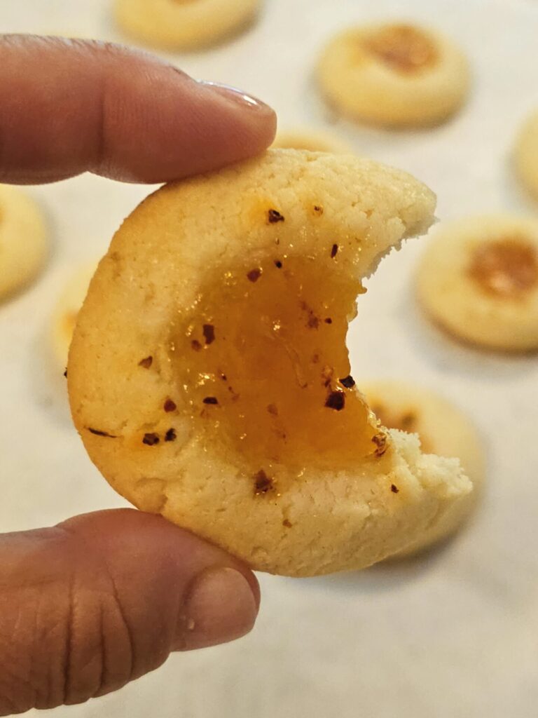 A hand holds up one of these Easy 2-Bite Mango Tajín Thumbprints from the side. A bite has been taken out of the cookie.