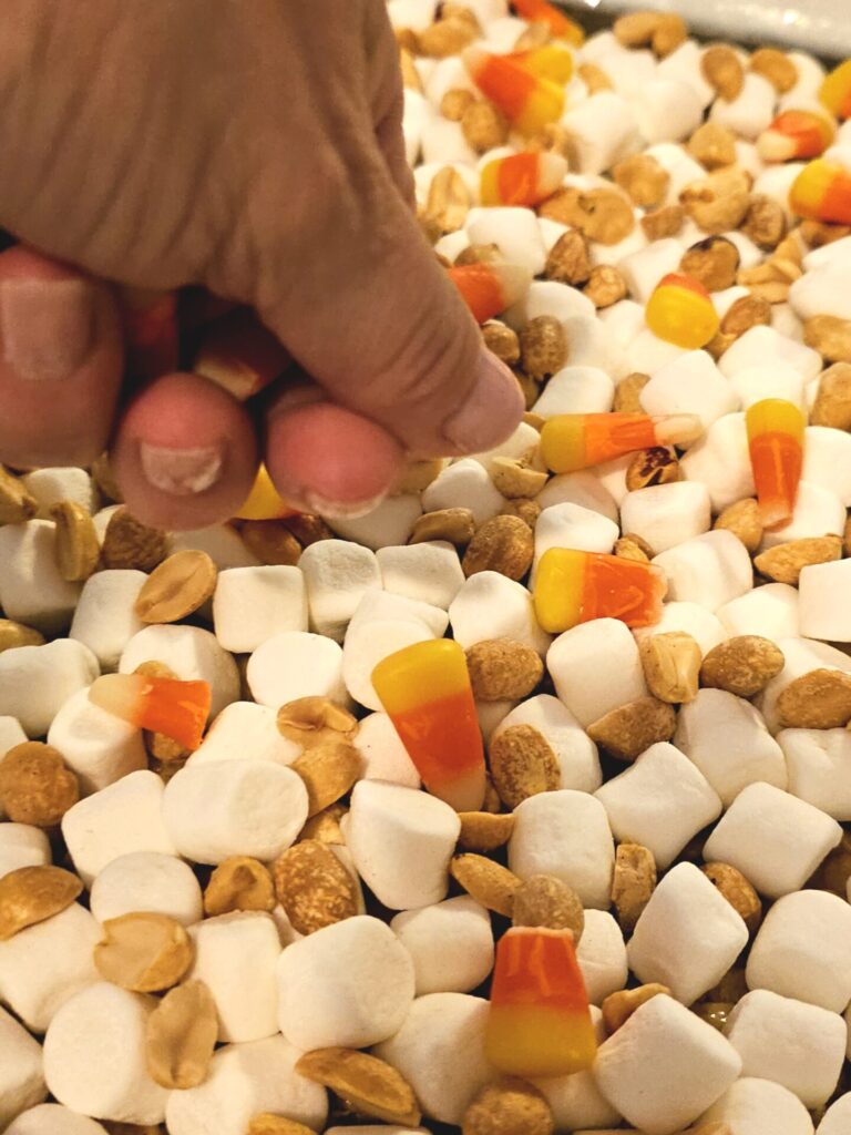 A hand holding a candy corn and peanuts tops these fall peanut butter rice krispie bars.