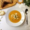 A bowl of Delicious Butternut Squash Soup in Under 1 Hour is topped with pepitas and cheese crumbles.