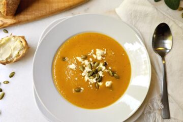 A bowl of Delicious Butternut Squash Soup in Under 1 Hour is topped with pepitas and cheese crumbles.