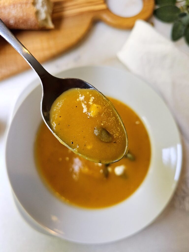 A bowl of Delicious Butternut Squash Soup in Under 1 Hour is topped with pepitas and cheese crumbles.