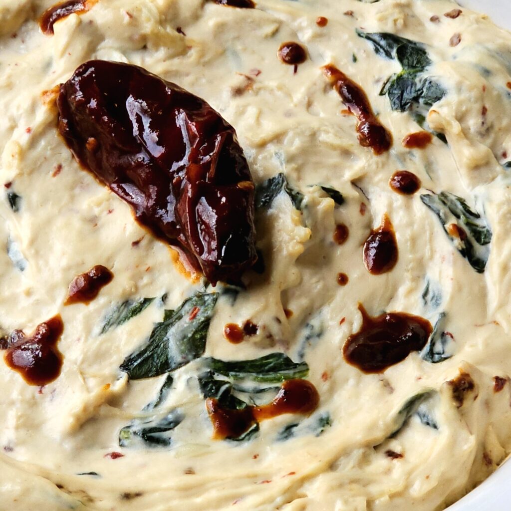 A closeup of a chipotle pepper sitting on top of a bowl of this Easy Chipotle Chicken Dip in 15 Minutes