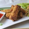 A plate of Irresistible Shrimp Egg Rolls in Under 1 Hour show off their crisp, fried shell. A cross cut shows a filling of vegetables and shrimp.
