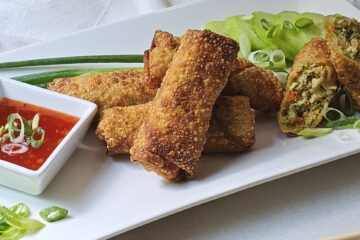 A plate of Irresistible Shrimp Egg Rolls in Under 1 Hour show off their crisp, fried shell. A cross cut shows a filling of vegetables and shrimp.