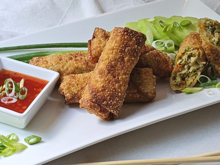A plate of Irresistible Shrimp Egg Rolls in Under 1 Hour show off their crisp, fried shell. A cross cut shows a filling of vegetables and shrimp.
