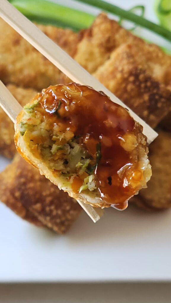 A close up shot of one of these Irresistible Shrimp Egg Rolls in Under 1 Hour show off their crisp, fried shell. A cross cut shows a filling of vegetables and shrimp.