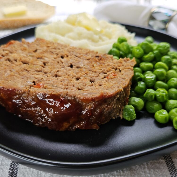 A slice of meatloaf, mashed potatoes, and peas are plated in this Easy Meatloaf Recipe photo.