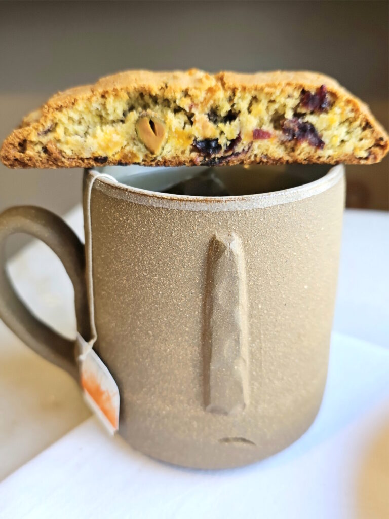 A single cranberry apricot biscotti is balanced across the top of a cup of tea.