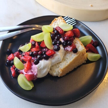 A slice of this Homemade Angel Food Cake is topped with fresh berries and whipped cream.