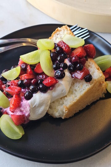 A slice of this Homemade Angel Food Cake is topped with fresh berries and whipped cream.