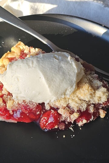 A slice of Old Fashioned Tart Cherry Pie is topped with a generous scoop of vanilla ice cream.