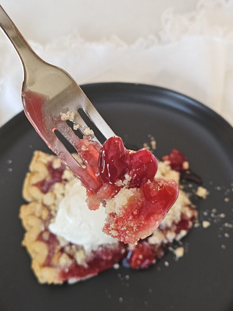 A slice of Old Fashioned Tart Cherry Pie is topped with a generous scoop of vanilla ice cream.