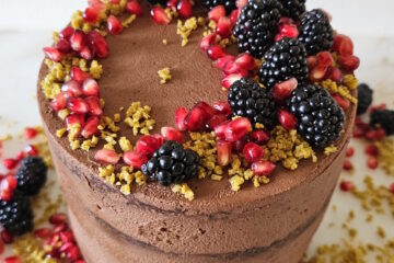 A finished Dubai Chocolate Cake standing four layers high is adorned with fresh fruit.