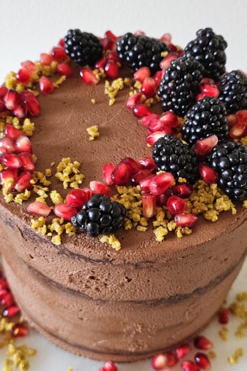 A finished Dubai Chocolate Cake standing four layers high is adorned with fresh fruit.