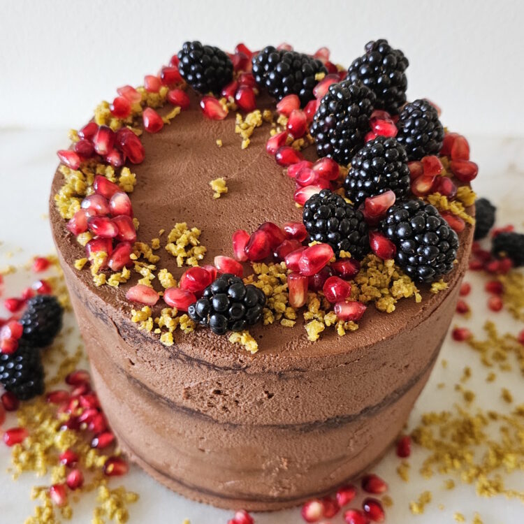 A finished Dubai Chocolate Cake standing four layers high is adorned with fresh fruit.