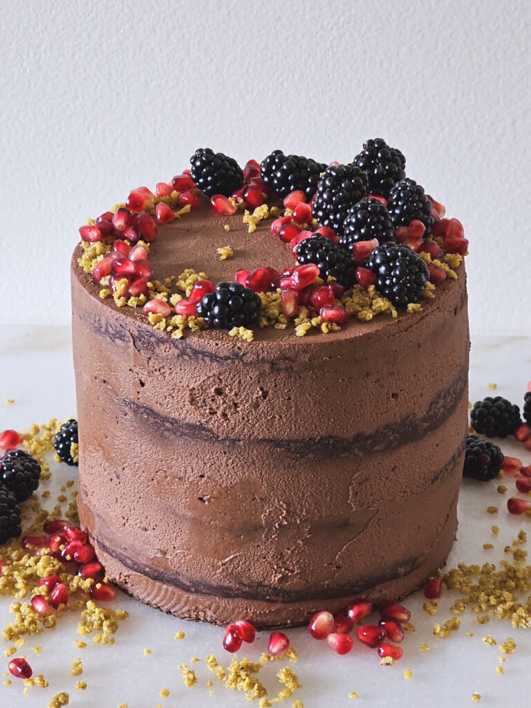 A finished Dubai Chocolate Cake standing four layers high is adorned with fresh fruit.