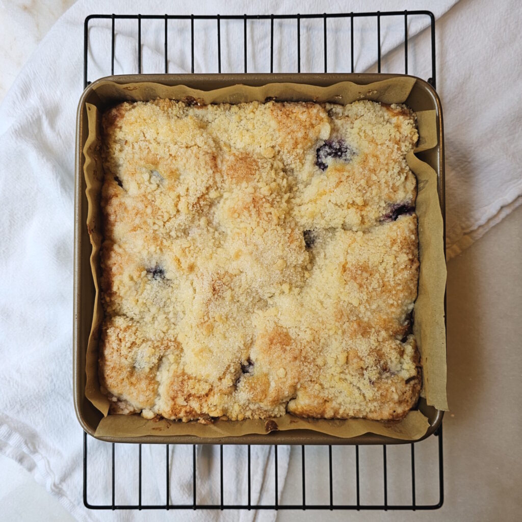 A fully-baked blackberry peach coffee cake sits on a cooling rack, waiting to be sliced into.
