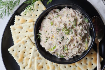 A small bowl is filled with this homemade tuna salad recipe. Saltine crackers are arranged on a plate.