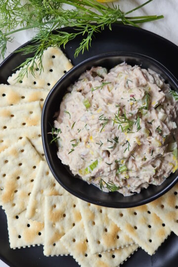A small bowl is filled with this homemade tuna salad recipe. Saltine crackers are arranged on a plate.