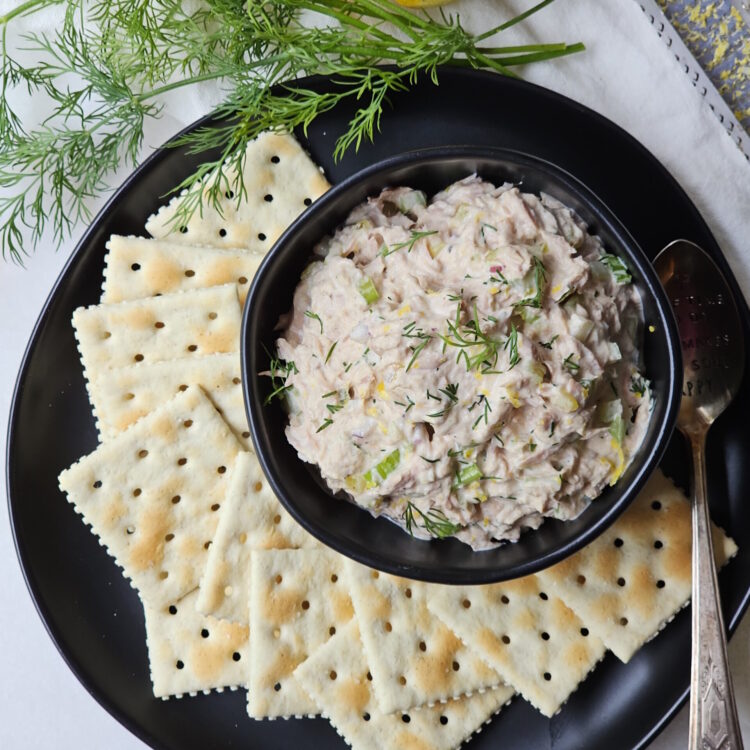 A small bowl is filled with this homemade tuna salad recipe. Saltine crackers are arranged on a plate.